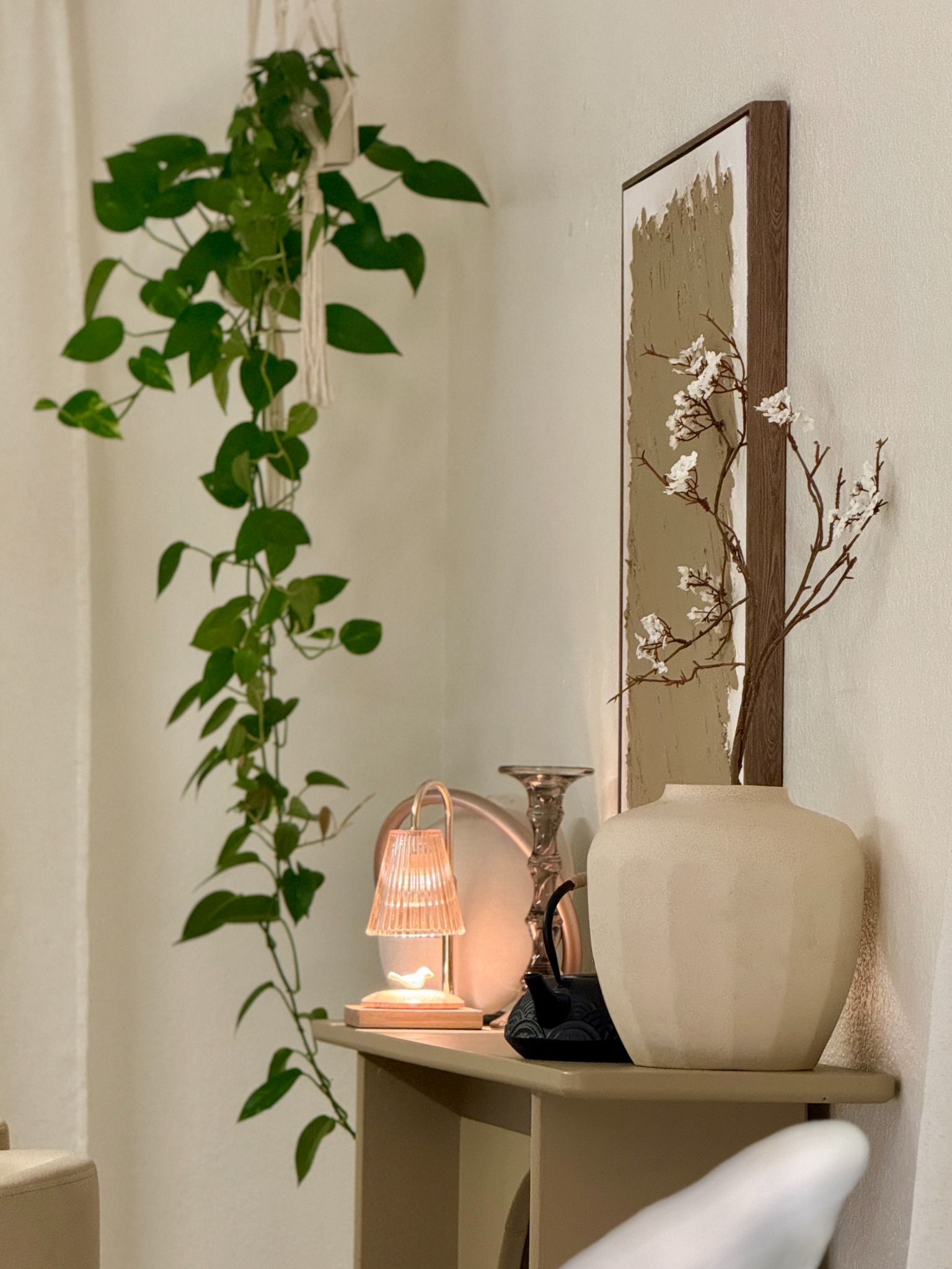 An intimate home vignette with trailing greenery, a warm lamp, art, and a sculptural vase