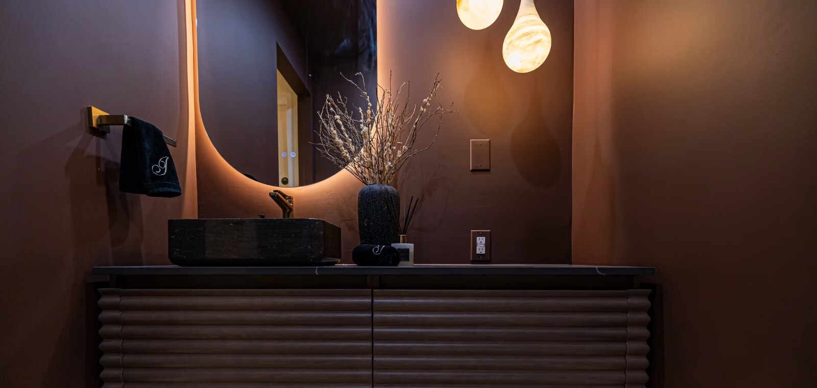 Dark sculptural bathroom vanity with warm ambient lighting